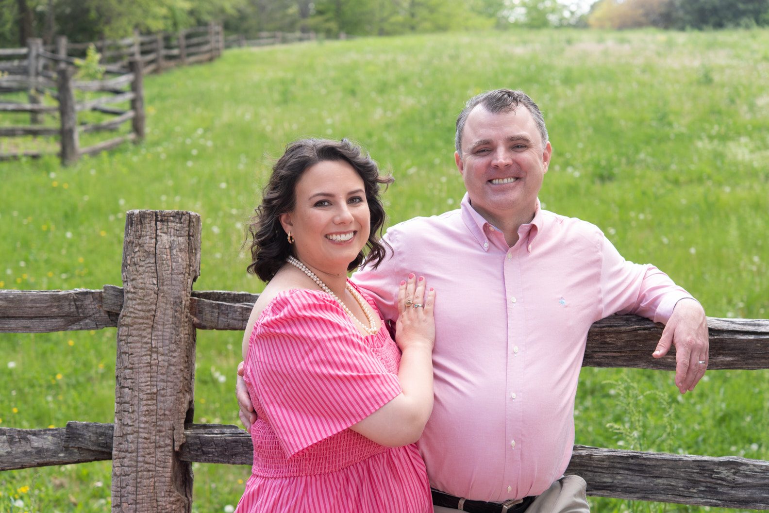 John and his wife at a wooden fence, Virginia countryside behind them.